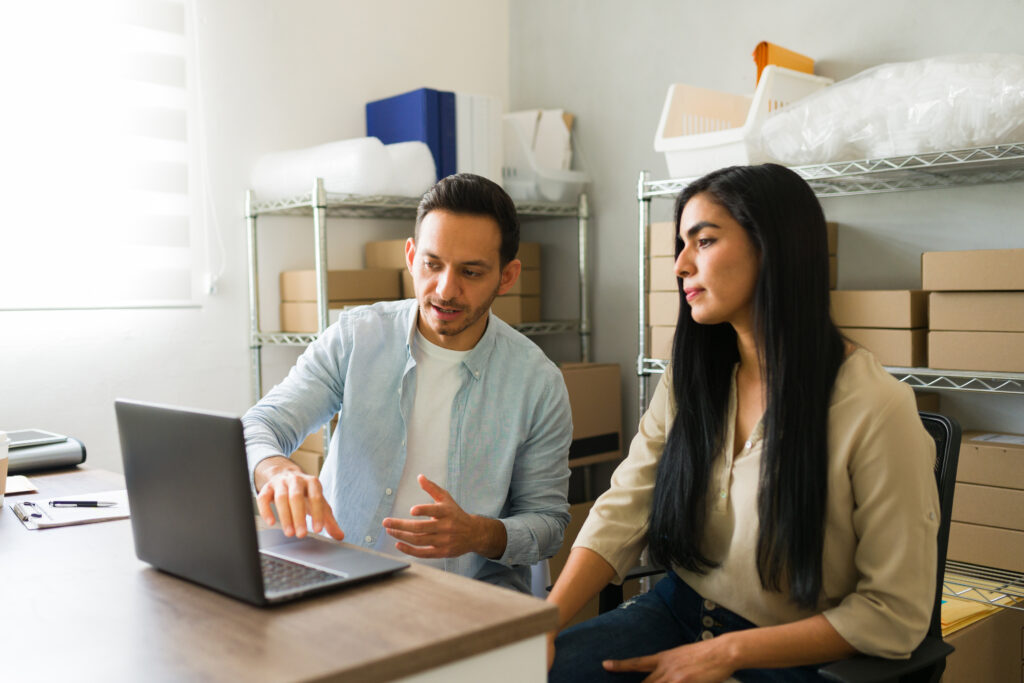 Two small business owners reviewing orders together in their stockroom, planning what their technology costs each month