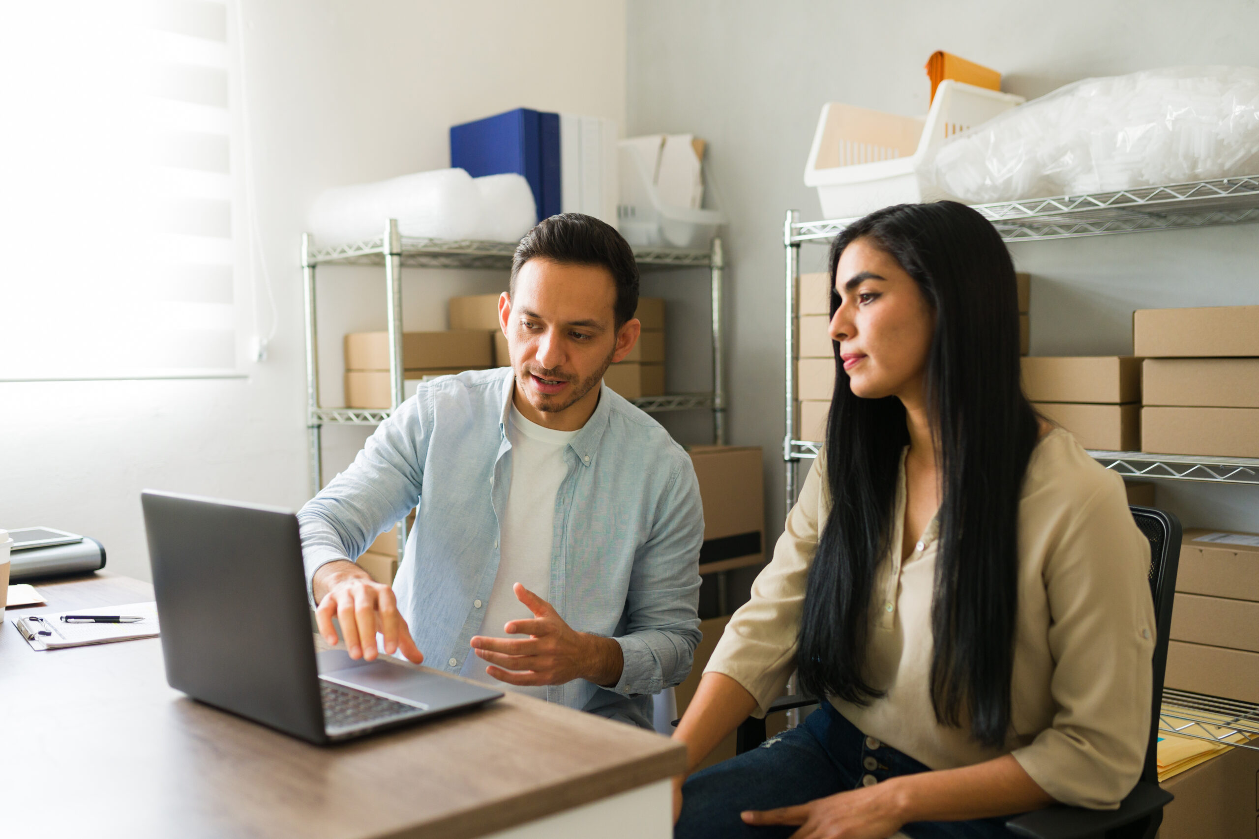 Two small business owners reviewing orders together in their stockroom, planning what their technology costs each month